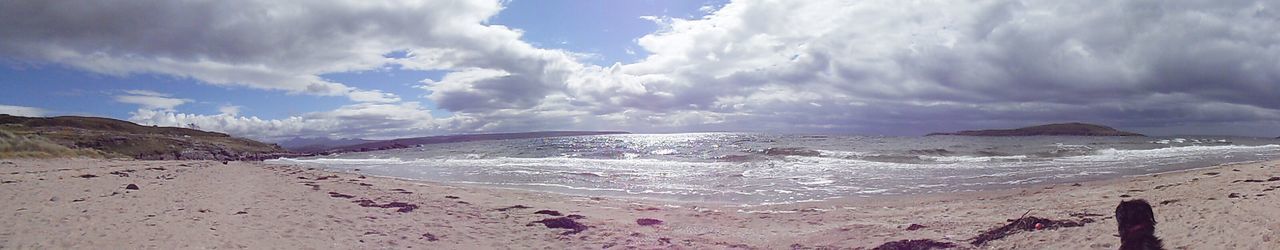 Panoramic shot of calm beach against clouds