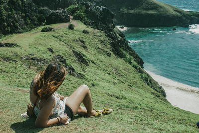 Woman sitting on grass by sea