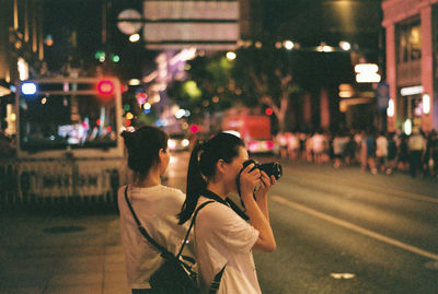 Woman photographing illuminated city street at night