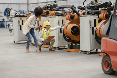 Engineer pointing at robotic arm discussing with businesswoman holding tablet pc in factory