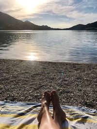 Low section of woman relaxing at beach against sky