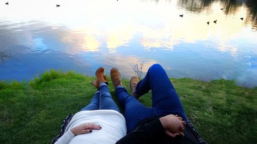 Low section of friends sitting on lake against sky