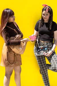 A girl giving face masks to another in the street with yellow background person