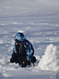 Playful boy sitting on snow covered field
