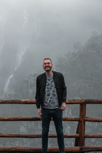 Portrait of smiling young man standing against mountains during winter