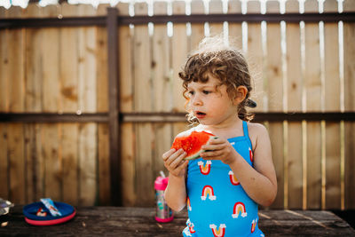 Close up of young girl sitting on picnic table eating watermelon