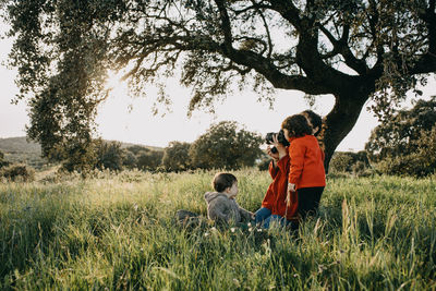 Mother with kids by tree on field against sky