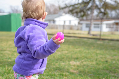 Rear view of boy holding pink flower on field