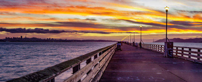 Pier on sea against cloudy sky at sunset