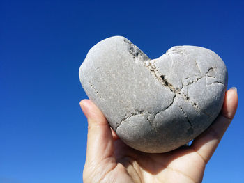 Close-up of hand holding heart shape on rock against clear blue sky