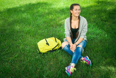 Young woman dressed in trendy jeans, a cardigan and with a backpack sitting in a city park 