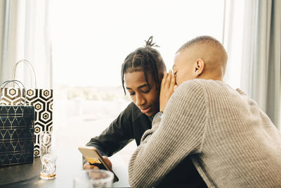 Teenage boy whispering into friend's ear while sitting in restaurant