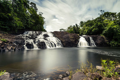 Scenic view of waterfall in forest against sky