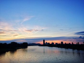 Silhouette buildings by river against sky during sunset