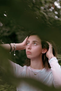 Young woman looking away while standing against trees