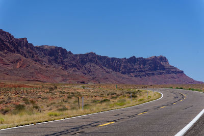 Road leading towards mountain against clear sky