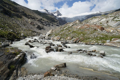 Scenic view of stream flowing through rocks against sky