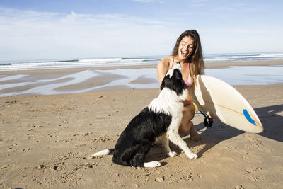 Happy woman with dog and surfboard on the beach