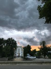 Road by buildings against cloudy sky