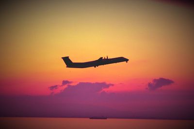 Silhouette airplane flying over sea against sky during sunset