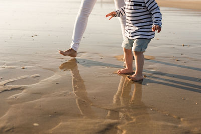 Low section of mother and son walking at beach