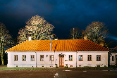 Low angle view of trees by building against sky at night