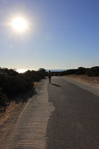 Rear view of woman walking on road against clear sky