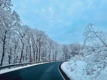 Road amidst snow covered trees against sky