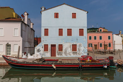 Boats moored on canal by buildings against sky