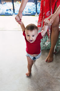 Mother holding hands of baby boy walking on floor at home