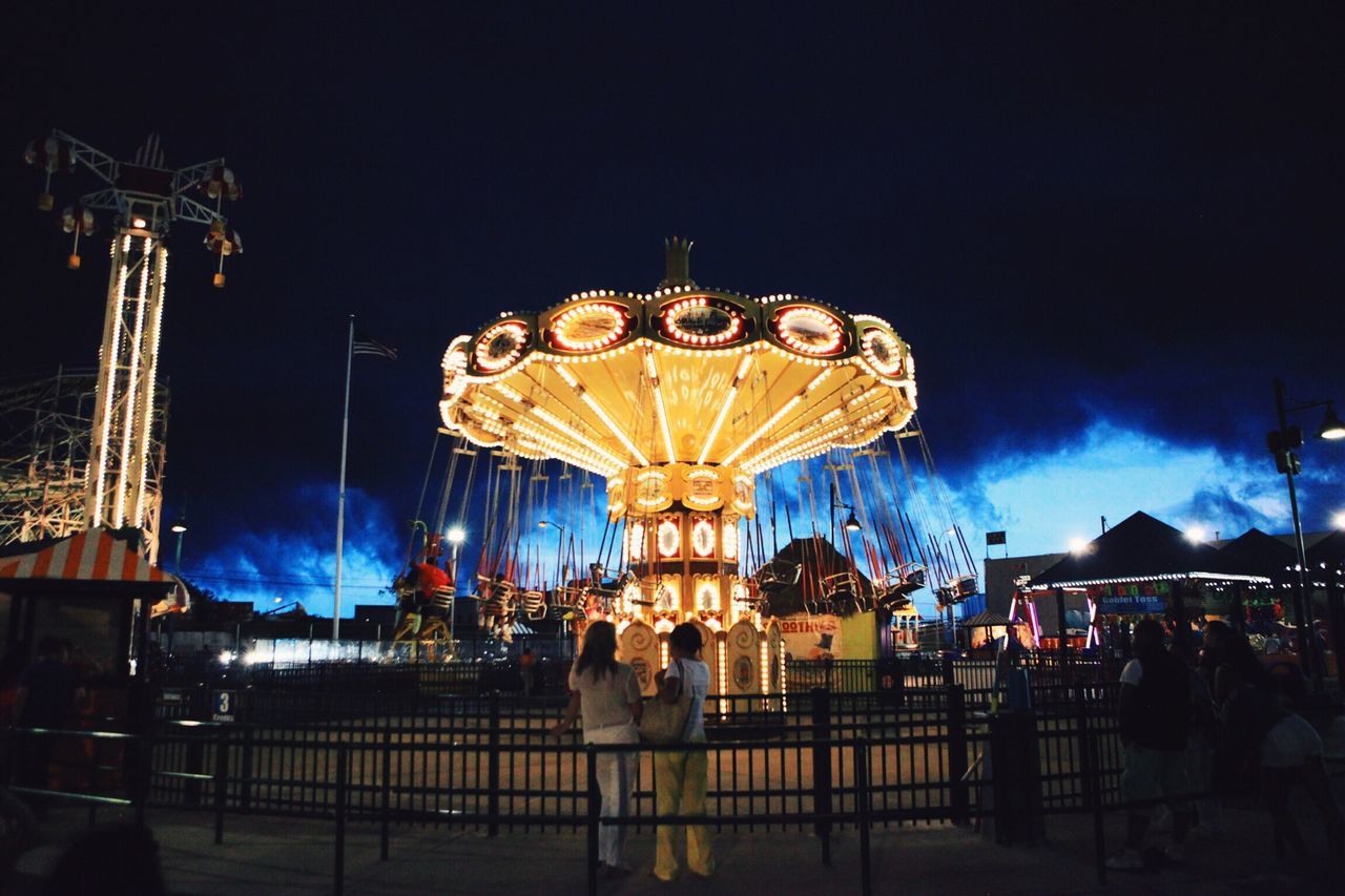 illuminated, lighting equipment, night, amusement park, decoration, low angle view, sky, arts culture and entertainment, hanging, amusement park ride, street light, carousel, built structure, incidental people, architecture, electric light, art, lantern, art and craft, in a row