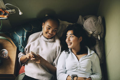 Directly above shot of smiling teenage girls listening music on mobile phone while lying on bed at home