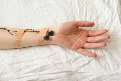 Cropped image of hand with headphones and bandages on bed