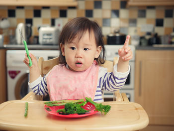 Baby girl with vegetables sitting on high chair at home