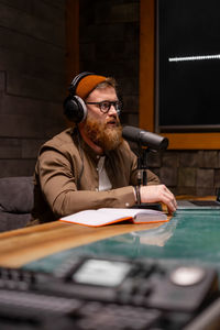 A man with a beard and headphones is seated at a table in front of a microphone