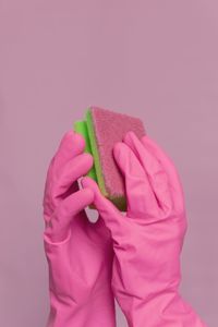 Cropped hands of person holding cleaning sponge against pink background