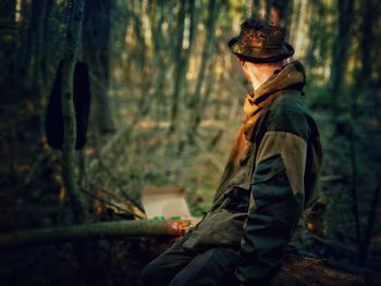 Side view of woman standing by tree in forest