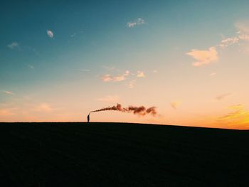 Silhouette person holding distress flare on field against sky during sunset