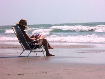 Woman relaxing on chair at beach against clear sky