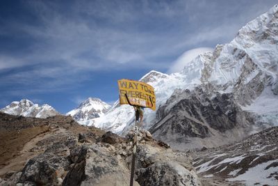 Yellow information sign on snowcapped mountains against sky during sunny day