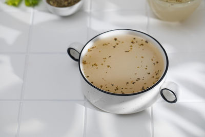 Healthy bone broth with spices in bowl on a white tile with a shadow pattern. 