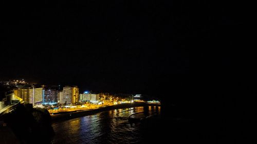 Illuminated buildings by river against clear sky at night