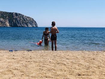 Rear view of shirtless boy on beach against clear sky