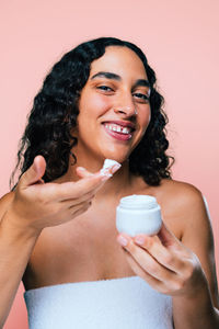 Portrait of young woman drinking glass against pink background