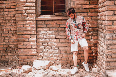 Young man looking down while standing against brick wall