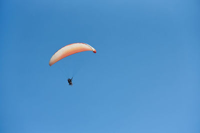 Low angle view of person paragliding against clear blue sky