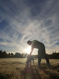 Man standing with his dog on field against sky during sunset