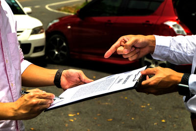 Midsection of man pointing at paper with insurance policy text on paper while standing by cars