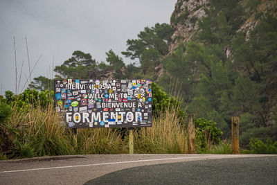 Information sign on road by trees in city against sky