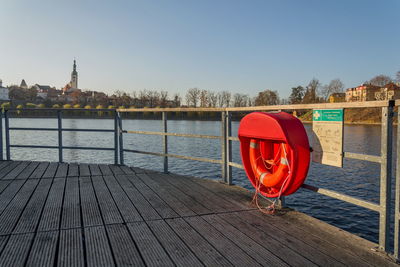 Red boat on pier by river against clear sky